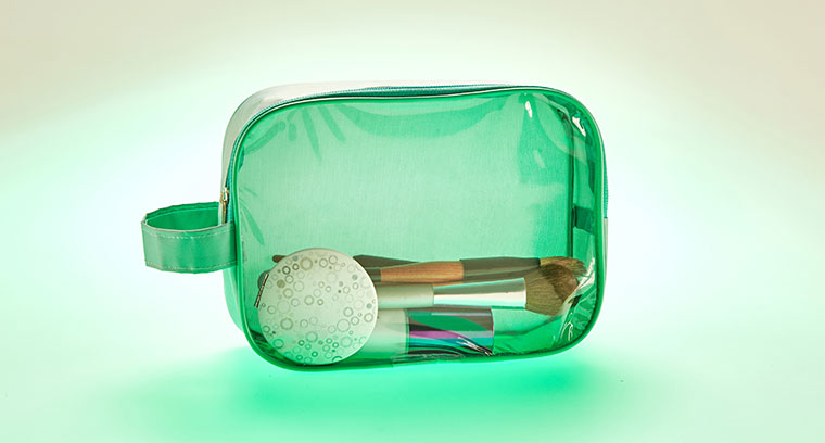 зеленая косметичка-пенал на молнии, лицевая сторона прозрачная из ПВХ/ПВД, остальное спанбонд, ручка на боку