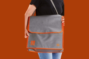 Обьемная промо сумка шоппер с крышкой клапаном и оранжевым логотипом на лицевой стороне, материал – серый спанбонд, окантовка – оранжевый спанбонд, длинная ручка на плечо – серый спанбонд.