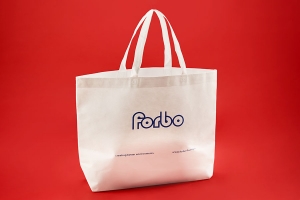 Промо сумка шоппер с логотипом сиреневого цвета из белого спанбонда, к низу у сумки появляется оббьем.
